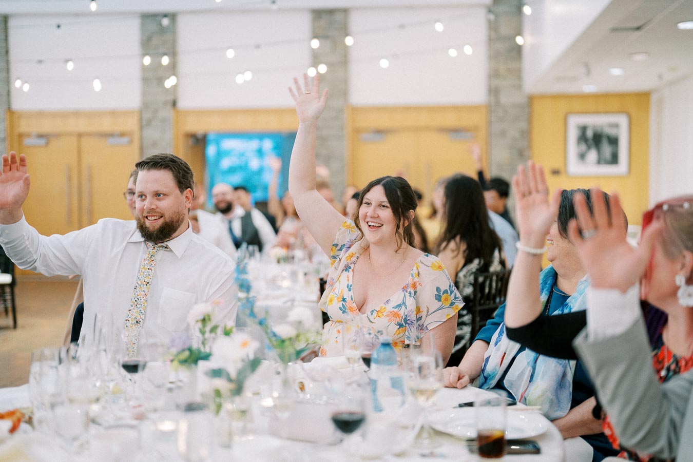 Guests at a formal event raise their hands in response to a question, creating a lively and engaging atmosphere.