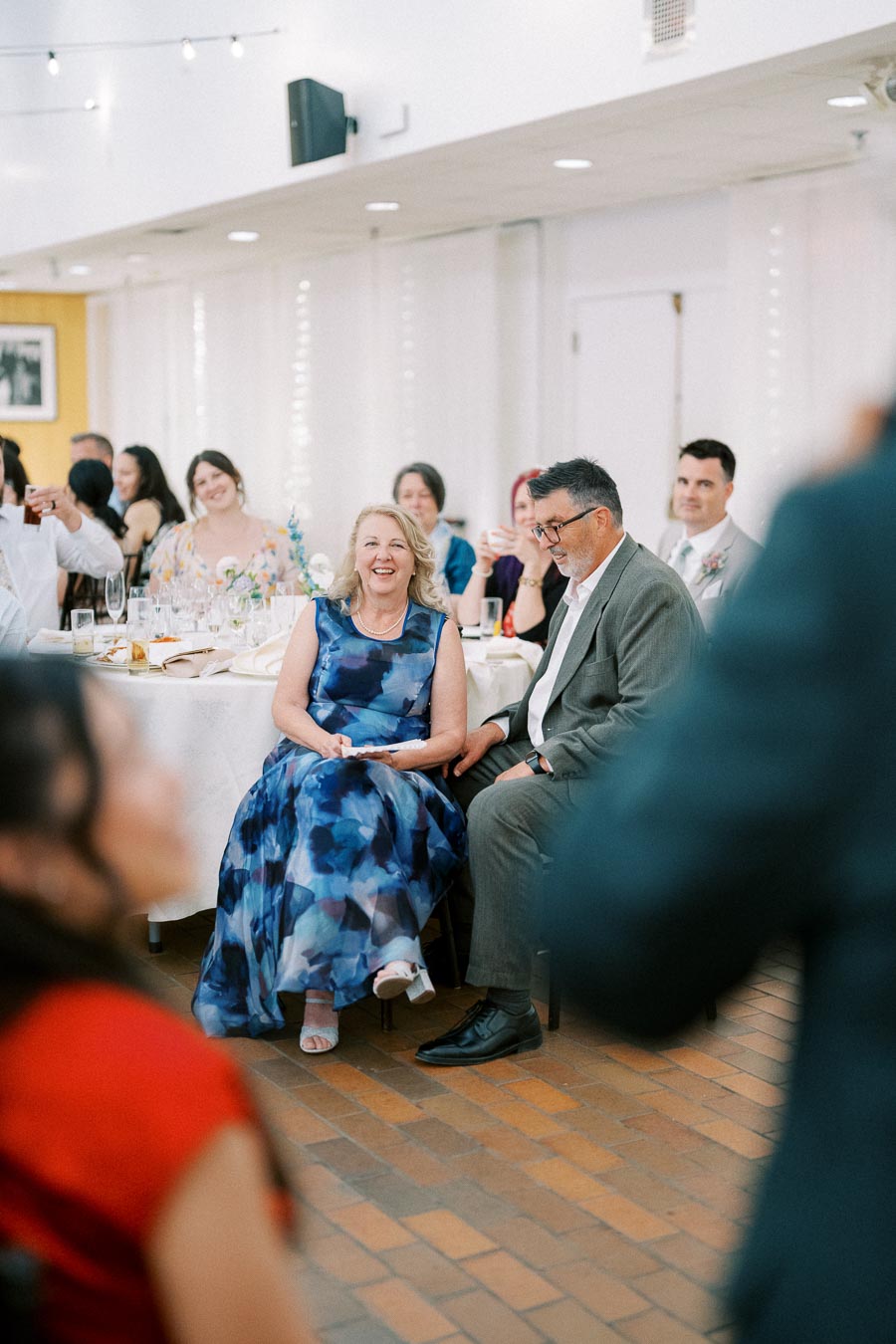 A joyful group of wedding guests seated at a reception table, with a woman in a blue dress smiling, capturing the joyful atmosphere of the celebration.