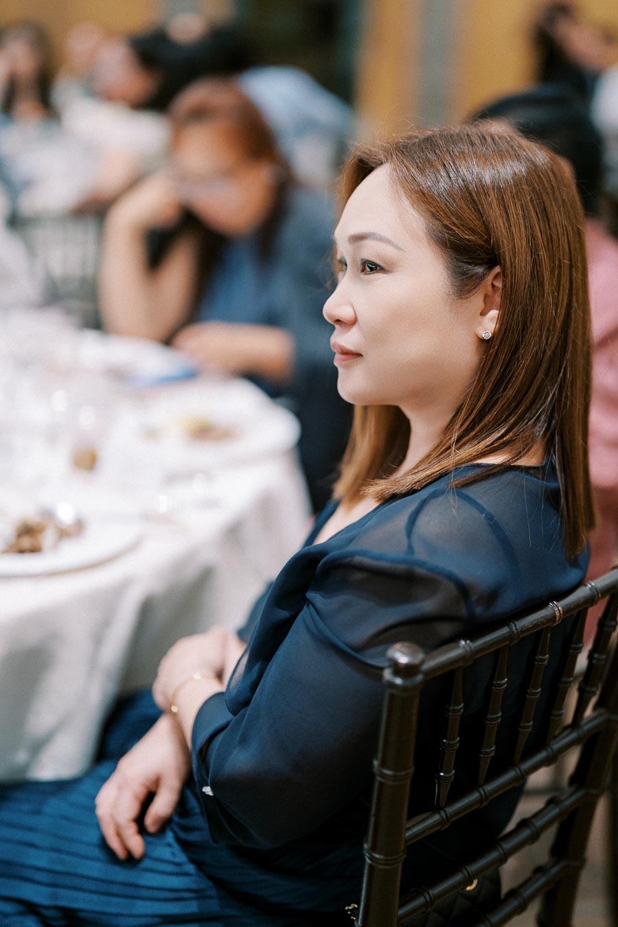 A woman in a blue blouse sitting at a dinner table during a formal event.