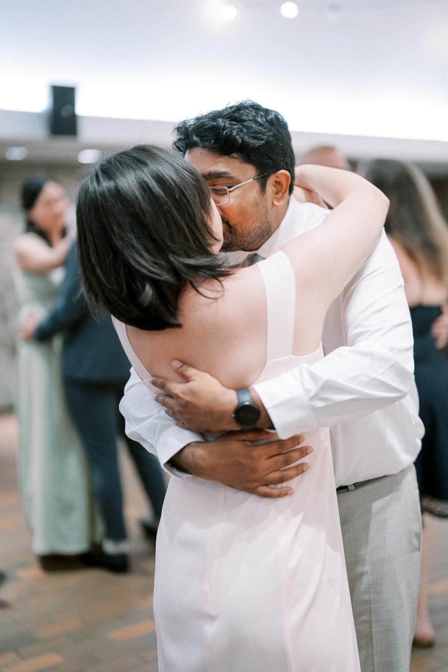 A couple sharing a tender moment on the dance floor, embracing each other closely during a wedding reception, with guests in the background.
