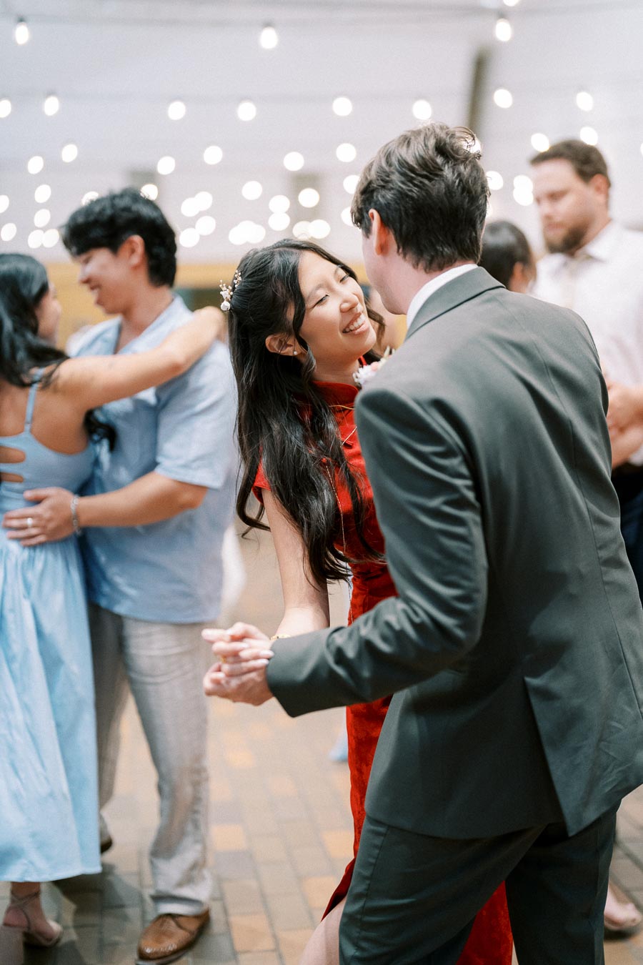 Couples joyfully dancing under string lights at a vibrant wedding reception, highlighting festive atmosphere and elegant attire.