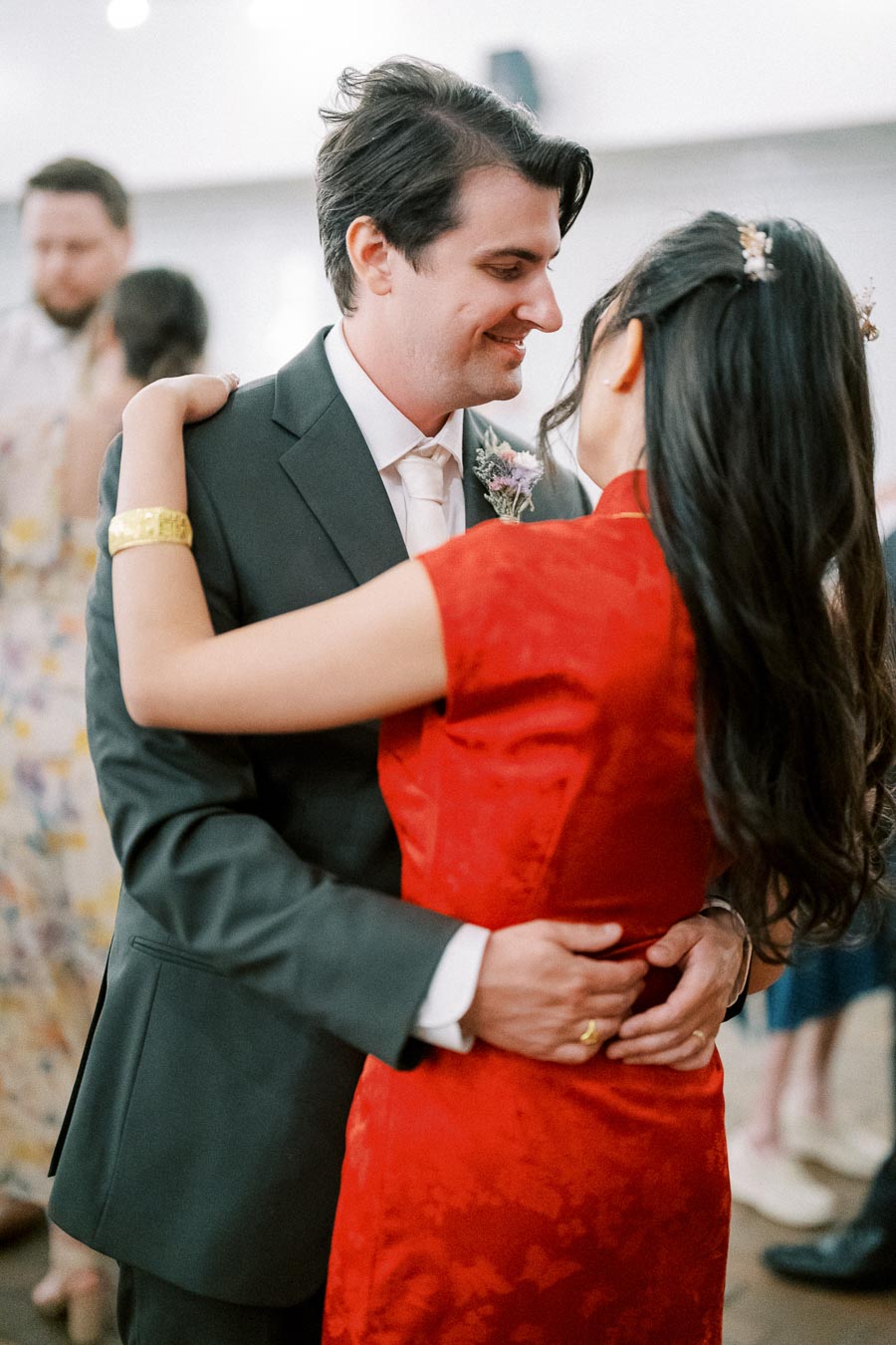 A couple dressed in formal attire shares a romantic moment while dancing at a wedding celebration, with the focus on their embrace and joyful expressions.