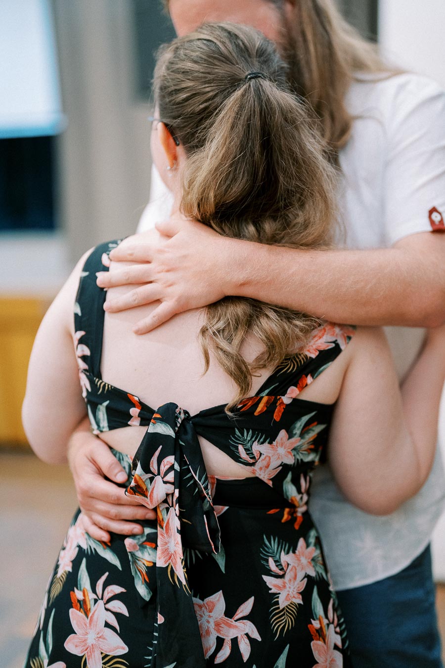A couple embracing closely, with focus on a woman wearing a black floral dress tied at the back.
