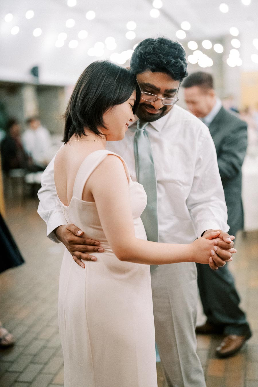 Couple sharing a tender dance at a wedding reception under warm string lights, capturing a romantic and joyful moment.
