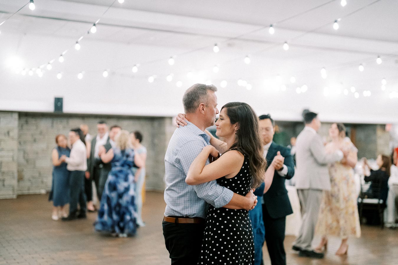 Couples dancing gracefully under string lights at an elegant indoor wedding reception, creating a romantic and joyful atmosphere.