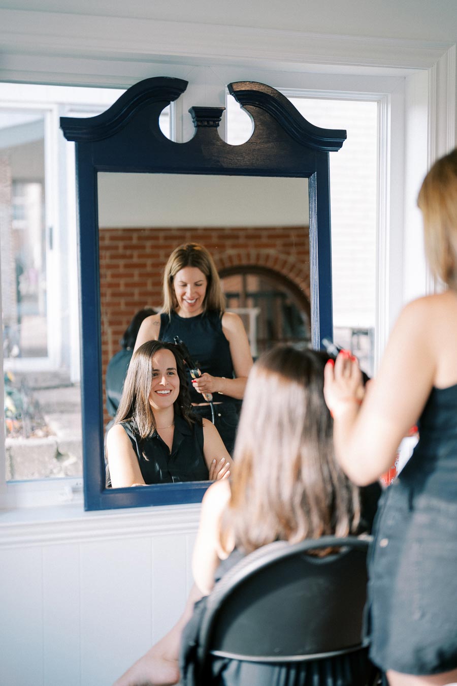 A woman smiling while getting a haircut in a salon, reflected in a mirror.