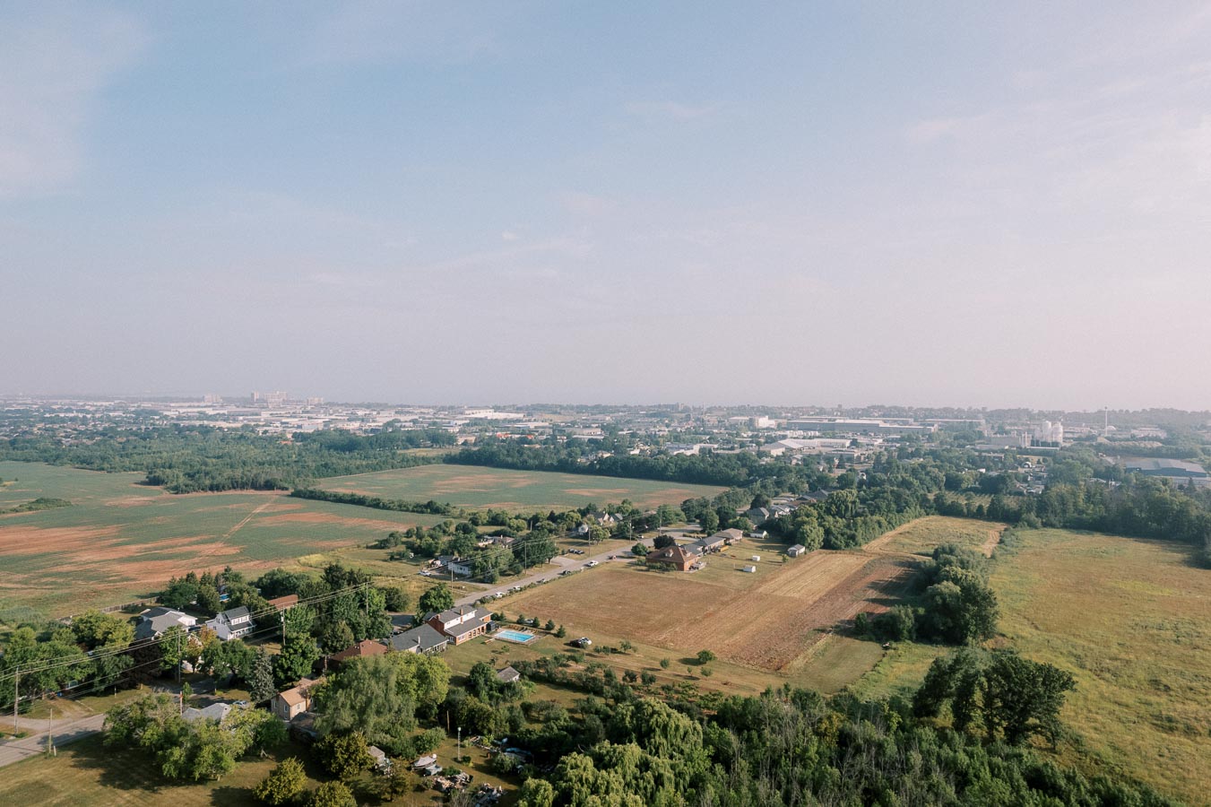 Aerial view of a rural landscape featuring expansive green fields and scattered houses under a clear blue sky.