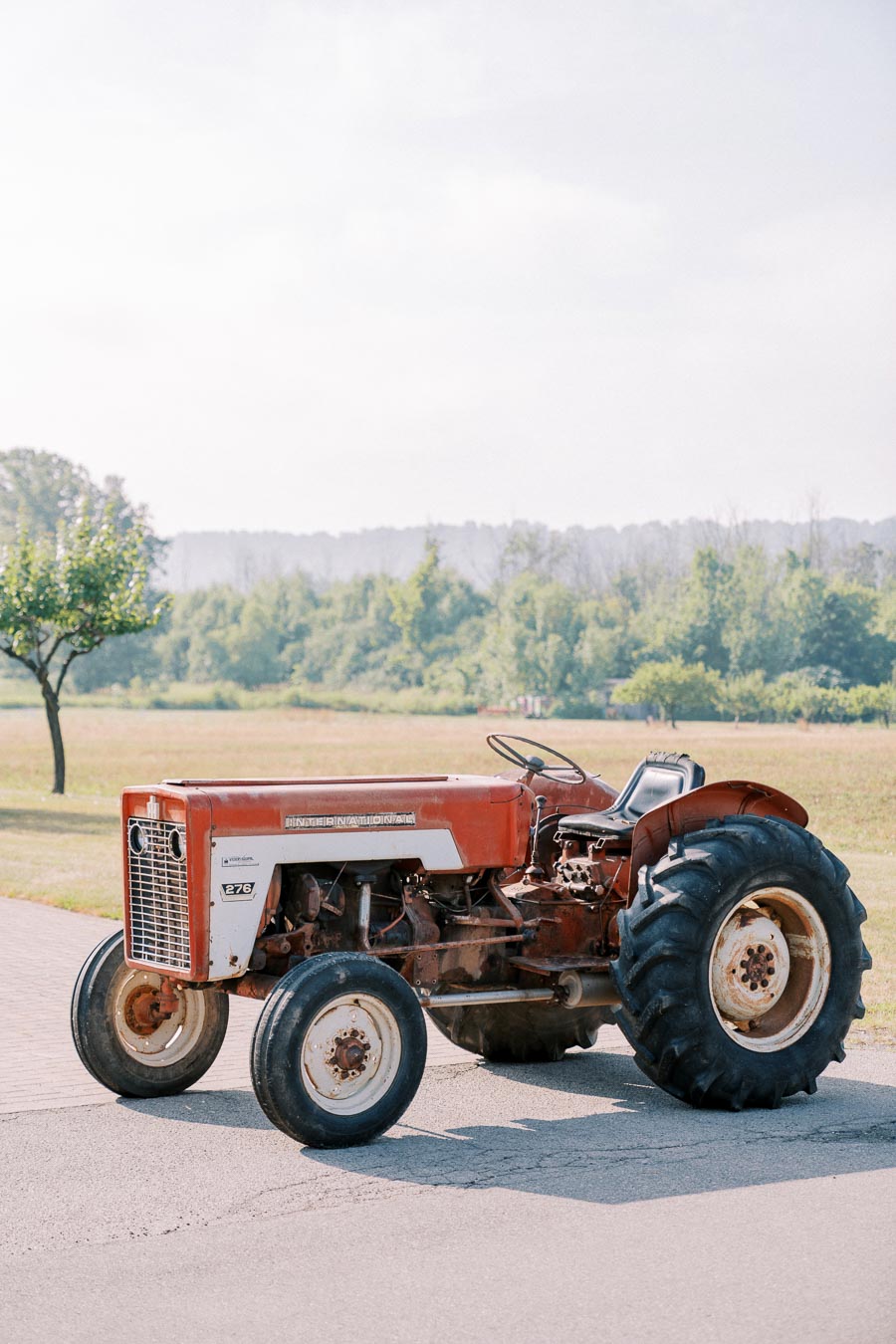 A rusty vintage tractor parked on a rural road with scenic countryside in the background, showcasing agricultural history and machinery.