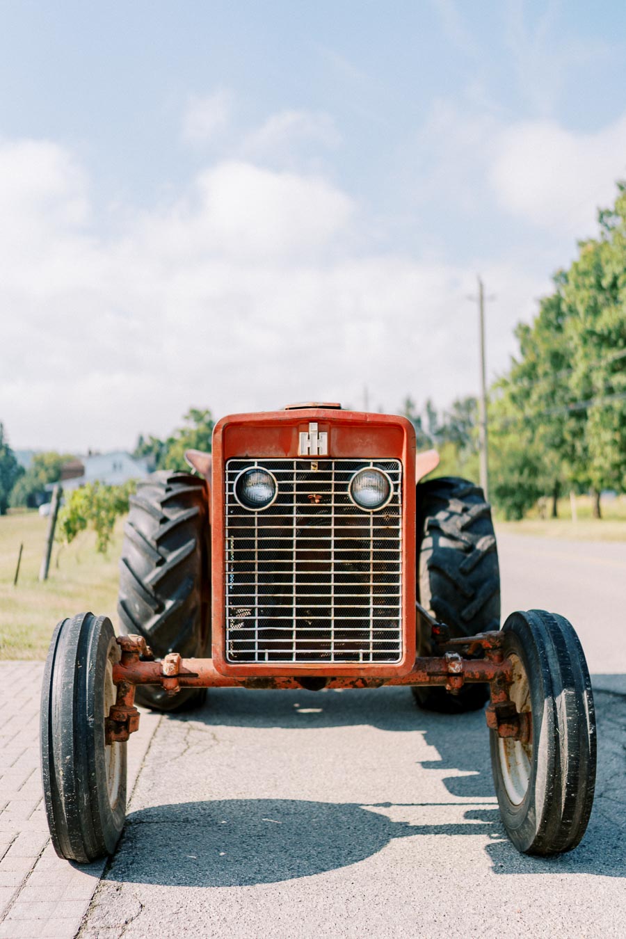 Red vintage tractor parked on a country road with a clear blue sky and green trees in the background.