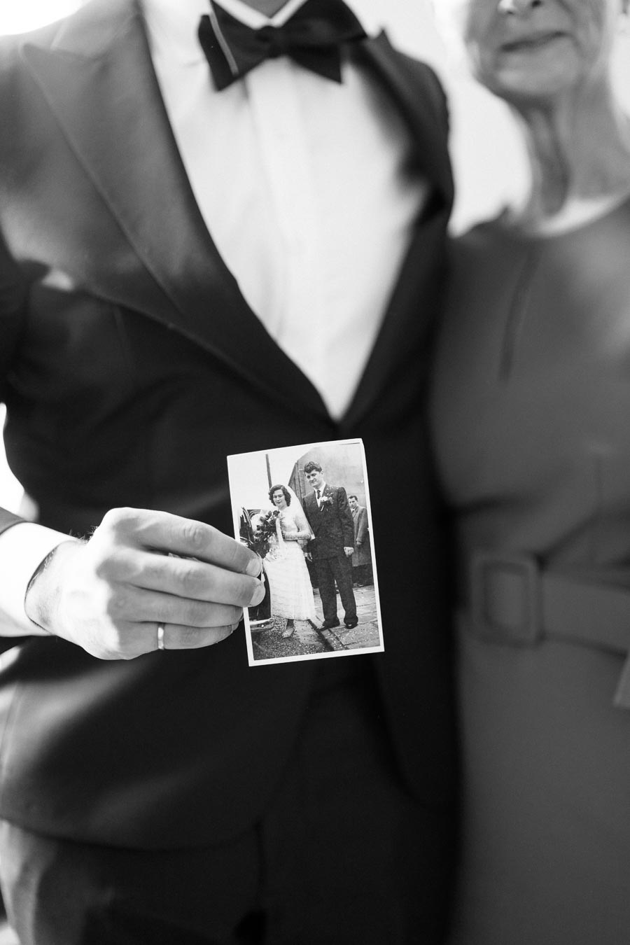 A person in formal attire holds a vintage wedding photo, symbolizing nostalgia and family memories.