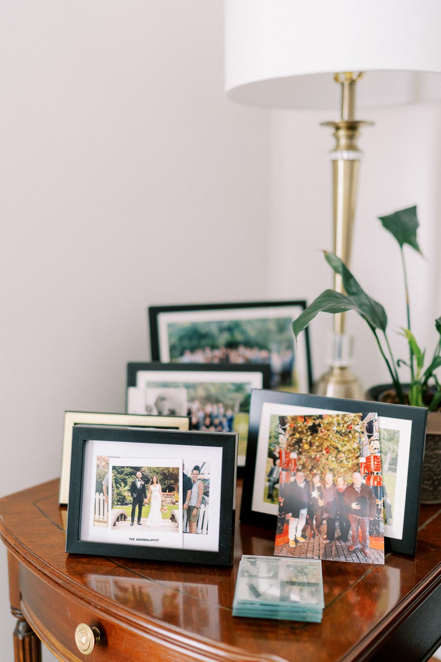 A collection of framed family photographs displayed on a wooden table, accompanied by a modern lamp and a potted plant, creating a cozy and personalized home decor setting.
