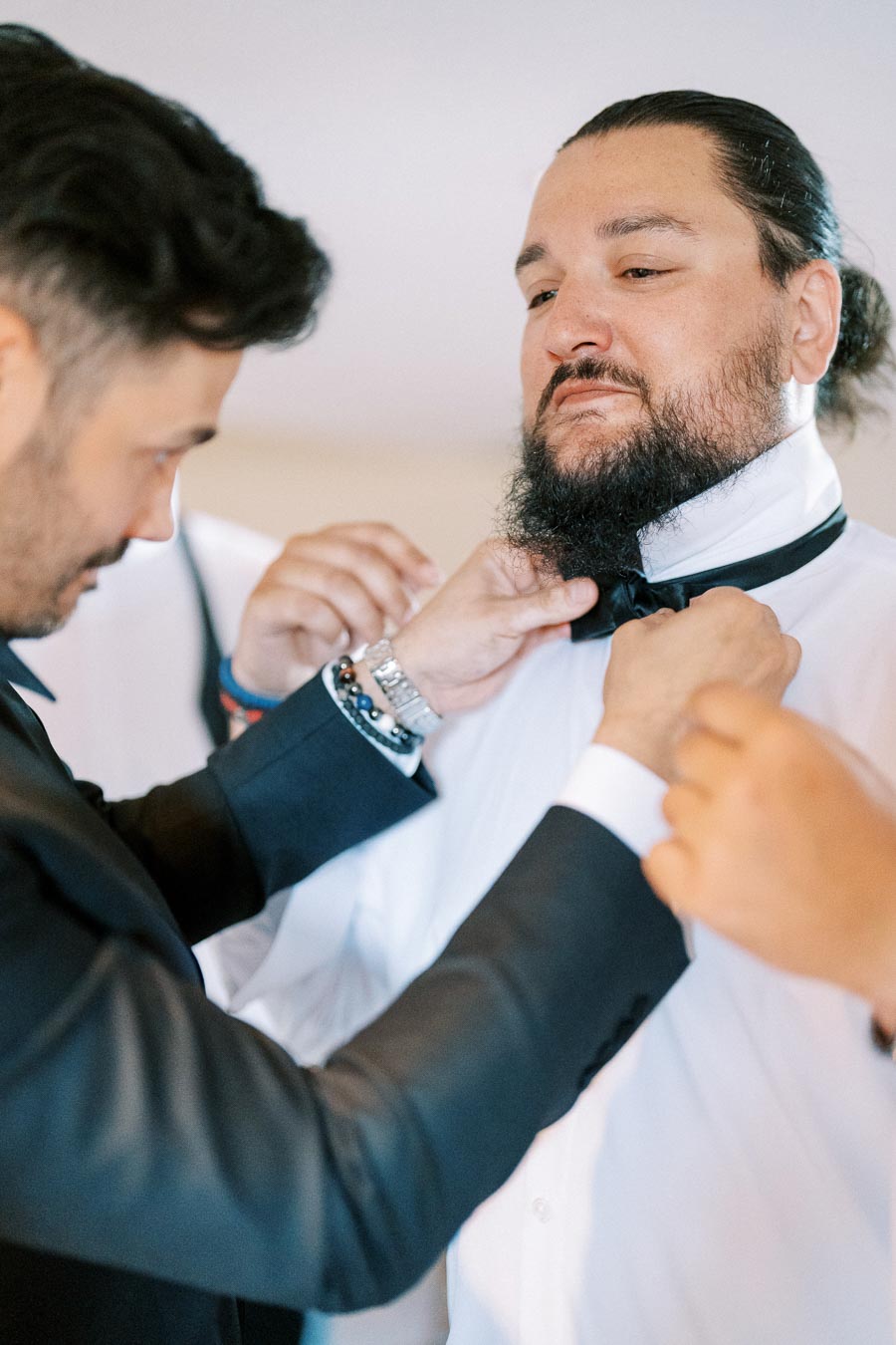 Groom getting ready on wedding day with friends adjusting his bow tie.