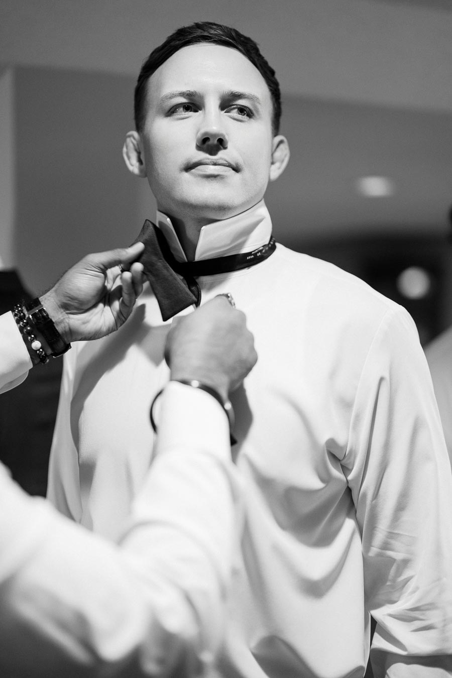 Black and white image of a person adjusting another person's bow tie, focusing on formal attire and preparation.