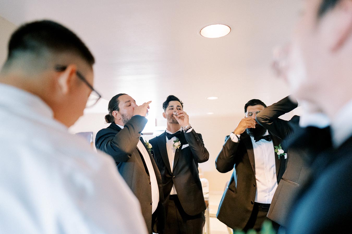Groomsmen in formal suits enjoying a celebratory drink before a wedding ceremony, capturing a candid and joyful pre-wedding moment.