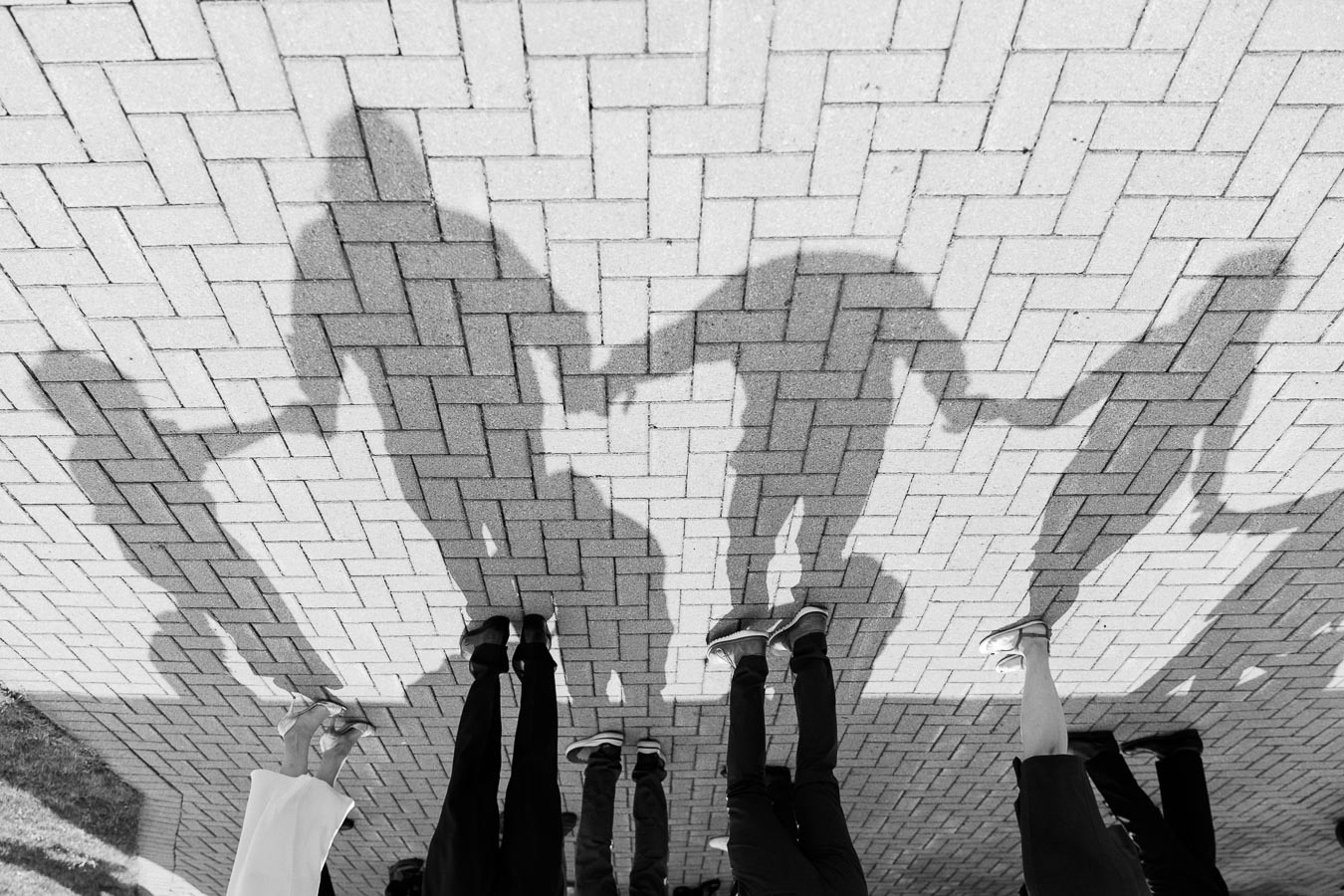 Shadows of people holding hands on a brick pavement, captured in black and white.