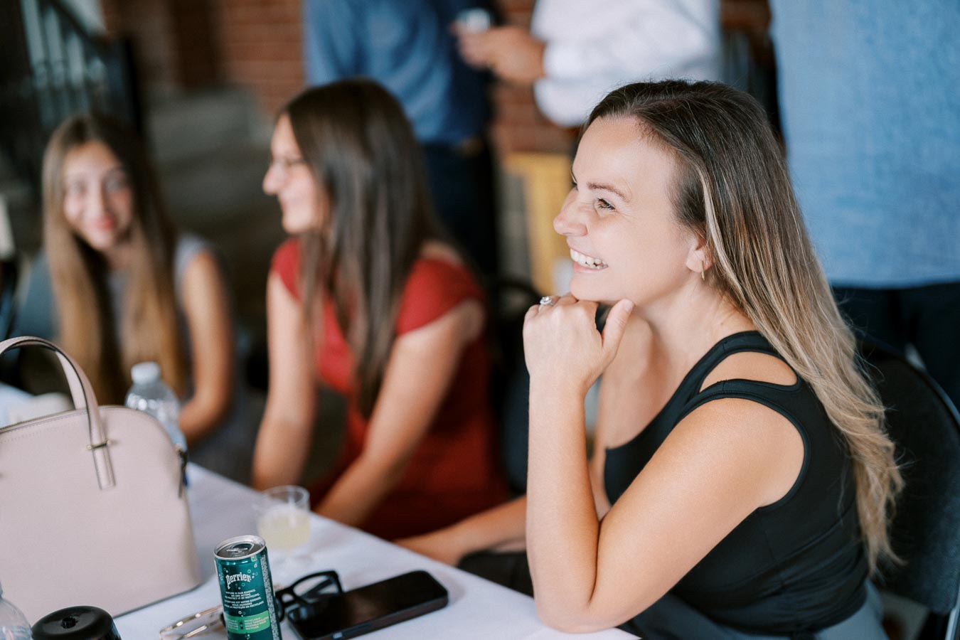 Group of women enjoying a social gathering at a table with drinks and a handbag, highlighting friendship and casual conversation.