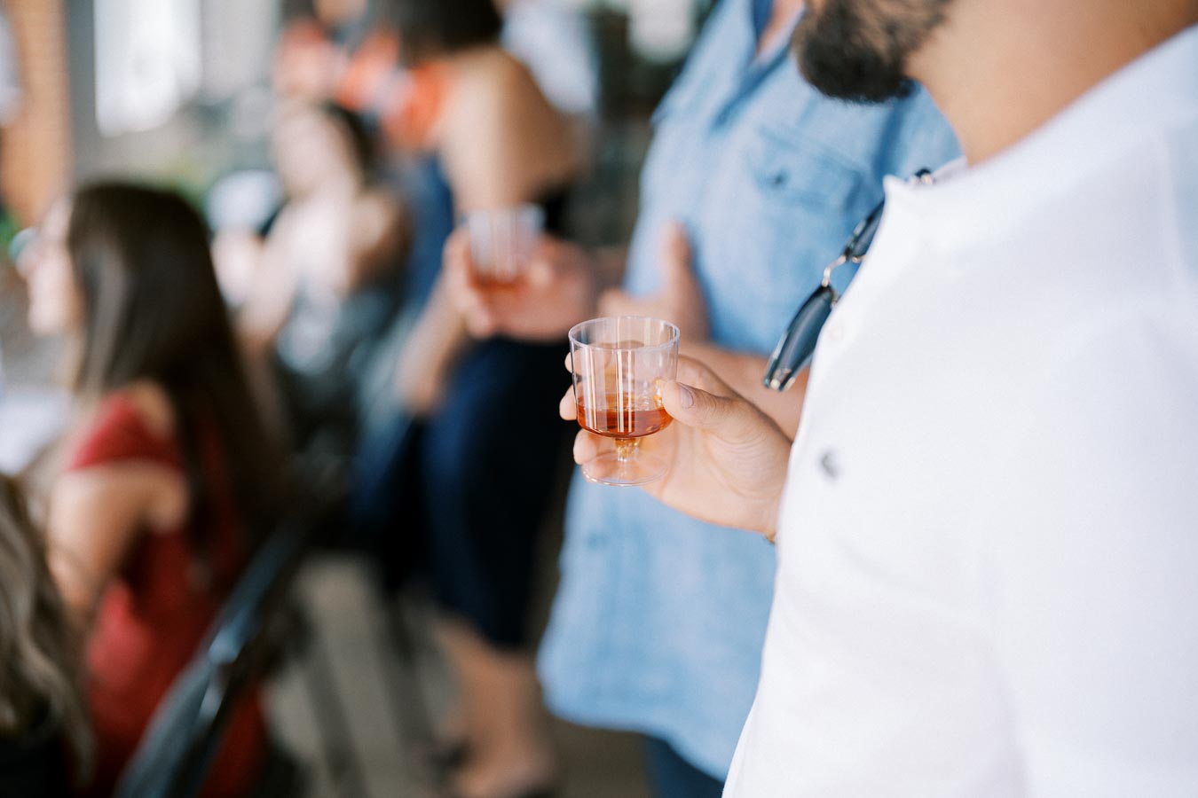 A group of people socializing at an event, holding cups with a beverage, wearing casual clothing, and enjoying a relaxed atmosphere indoors.
