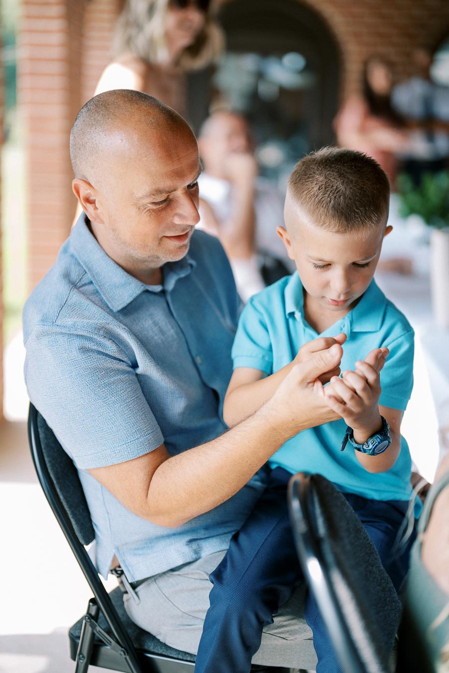 Father and son bonding in a casual setting, with the dad holding the child on his lap while engaging in a shared activity.