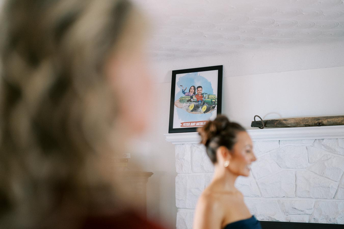 A woman in focus near a white stone fireplace with a framed cartoon artwork on the mantel.