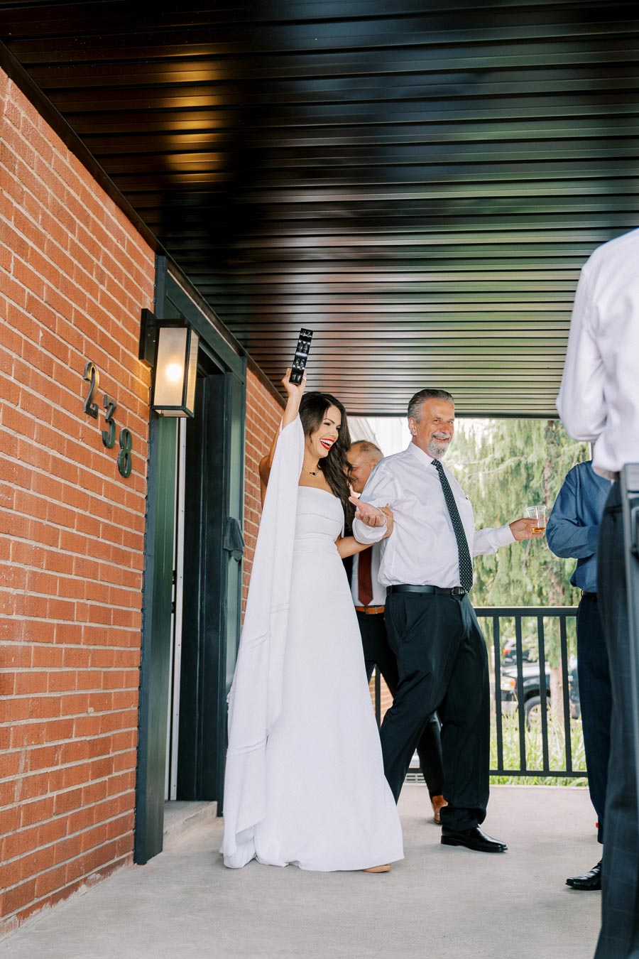 Woman in white wedding dress celebrating with guests on a porch.