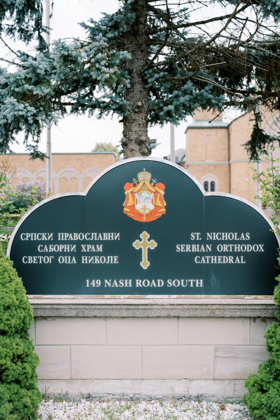 Sign at St. Nicholas Serbian Orthodox Cathedral, 149 Nash Road South, surrounded by greenery and a tree, emphasizing architectural heritage and religious significance.
