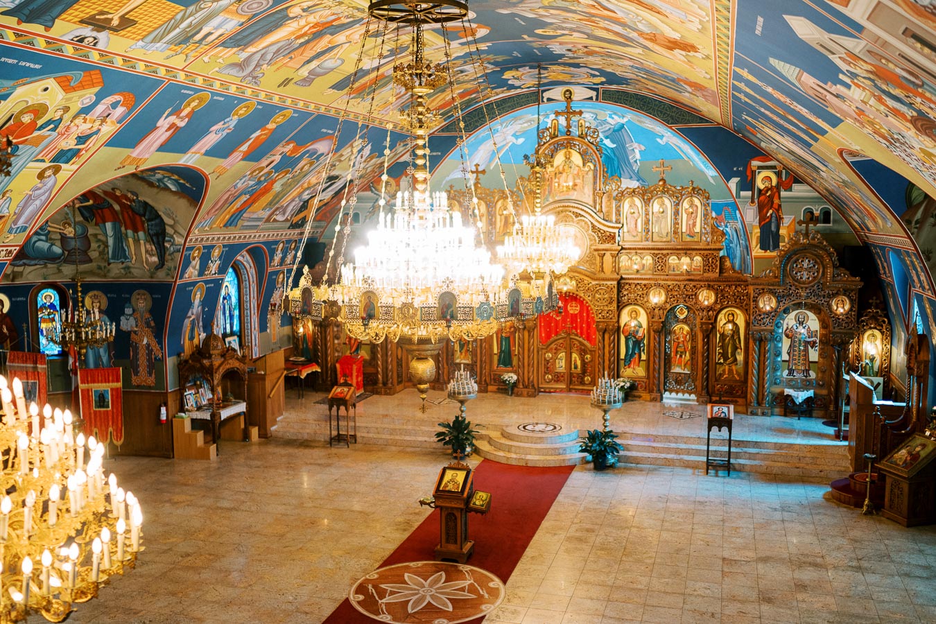 Interior of a beautifully decorated Orthodox church with intricate iconography, large chandeliers, and ornate woodwork. The ceiling and walls are adorned with colorful religious frescoes, creating a vibrant and spiritual atmosphere.