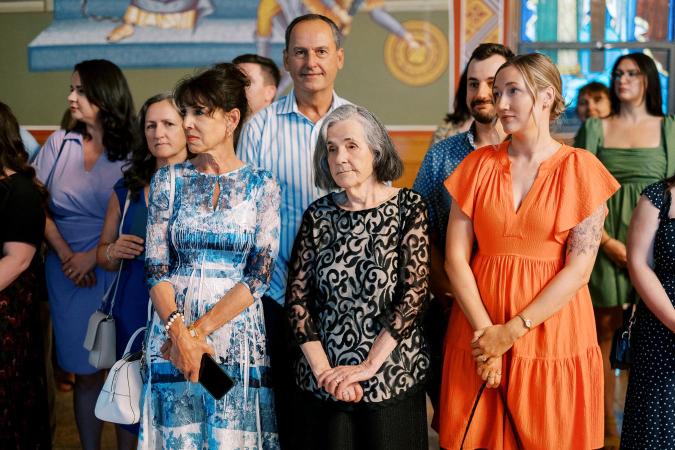 A group of people attending an indoor event, featuring a diverse mix of individuals wearing colorful and patterned clothing, standing in a richly decorated room.