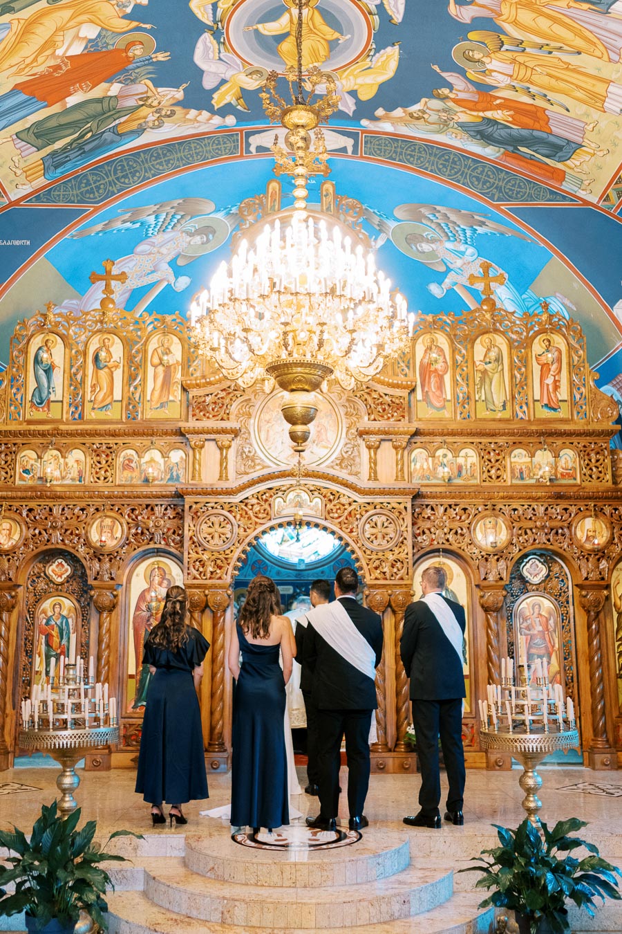 A group of people standing in front of an ornate altar in a beautifully decorated church, featuring intricate religious icons and a grand chandelier.