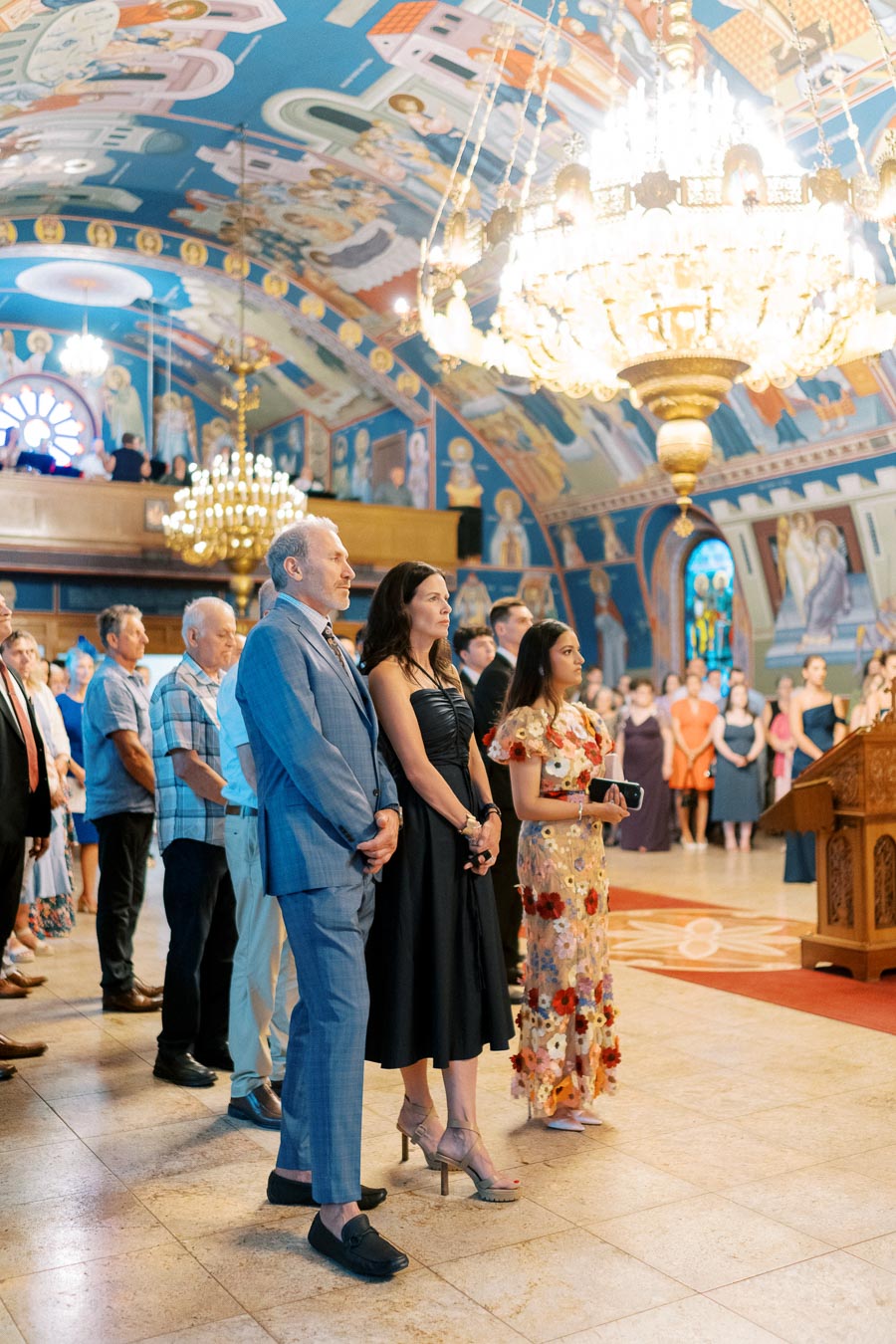 People attending a ceremony inside an ornately decorated church, featuring vibrant murals and large chandeliers.