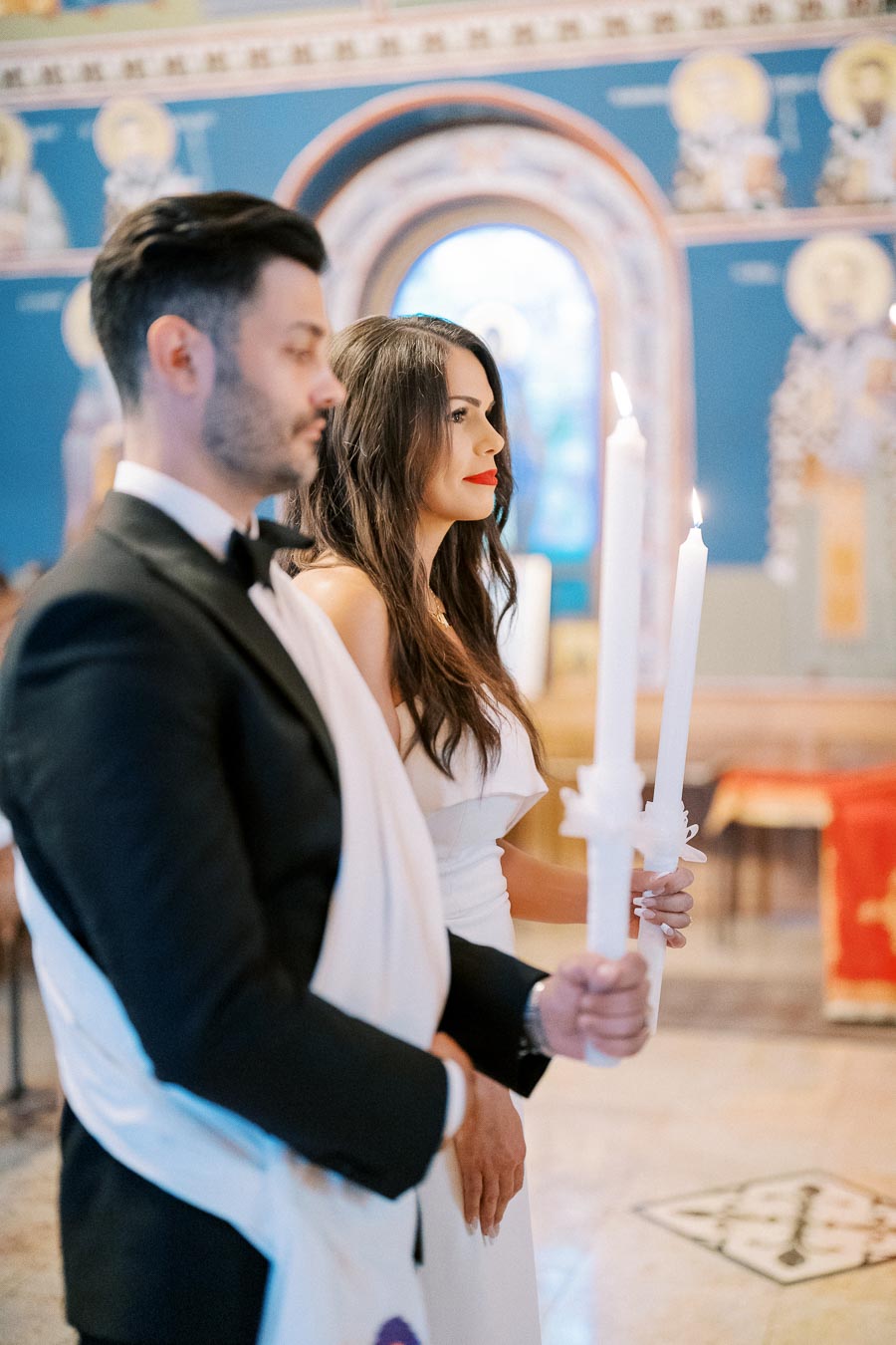 A couple holding candles during a wedding ceremony in an ornately decorated church.