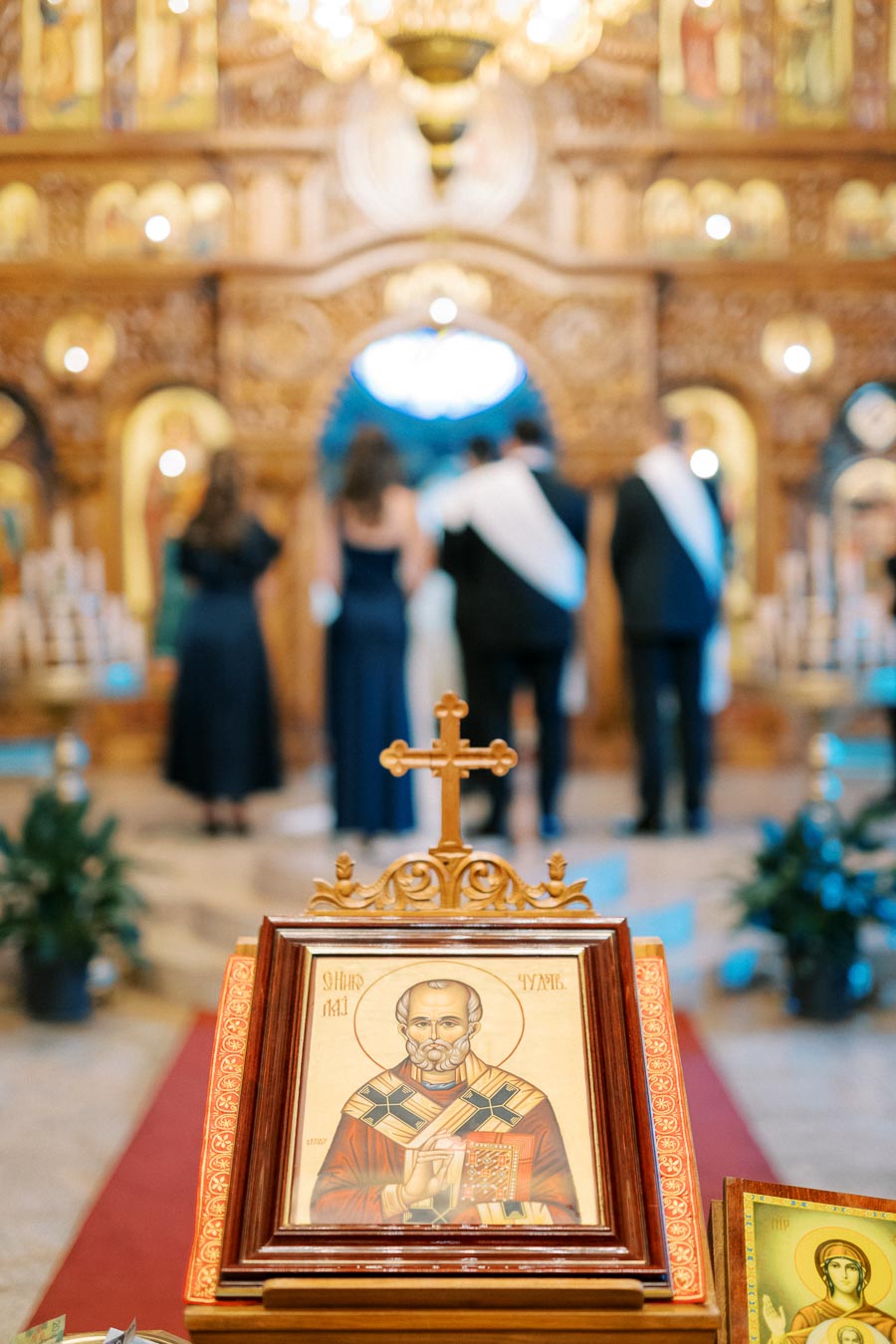 Orthodox wedding ceremony with a religious icon and cross in the foreground at a beautifully decorated church.