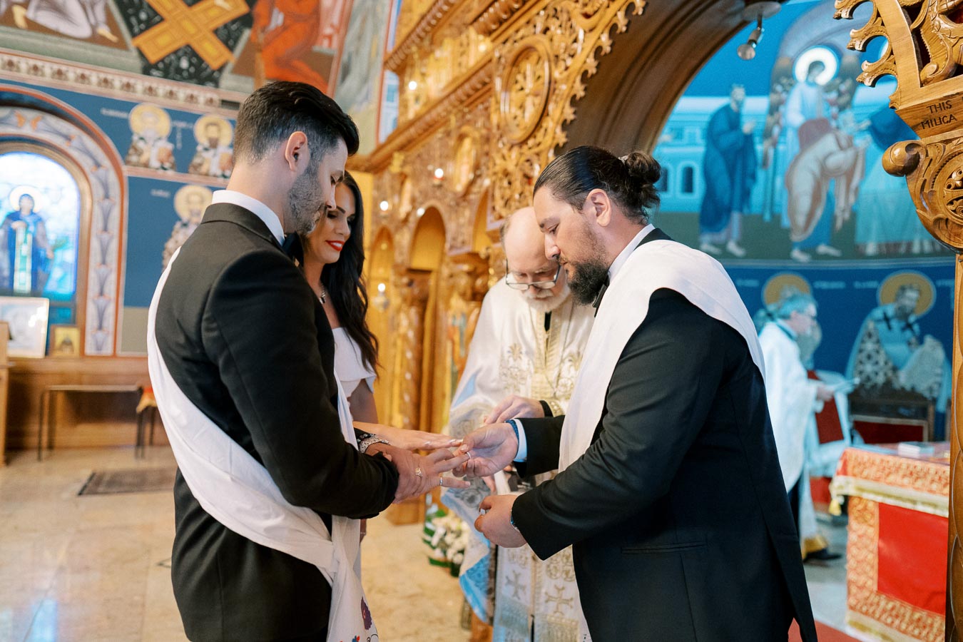 A couple participating in a traditional wedding ceremony inside a beautifully decorated church, with ornate wooden carvings and religious icons in the background.