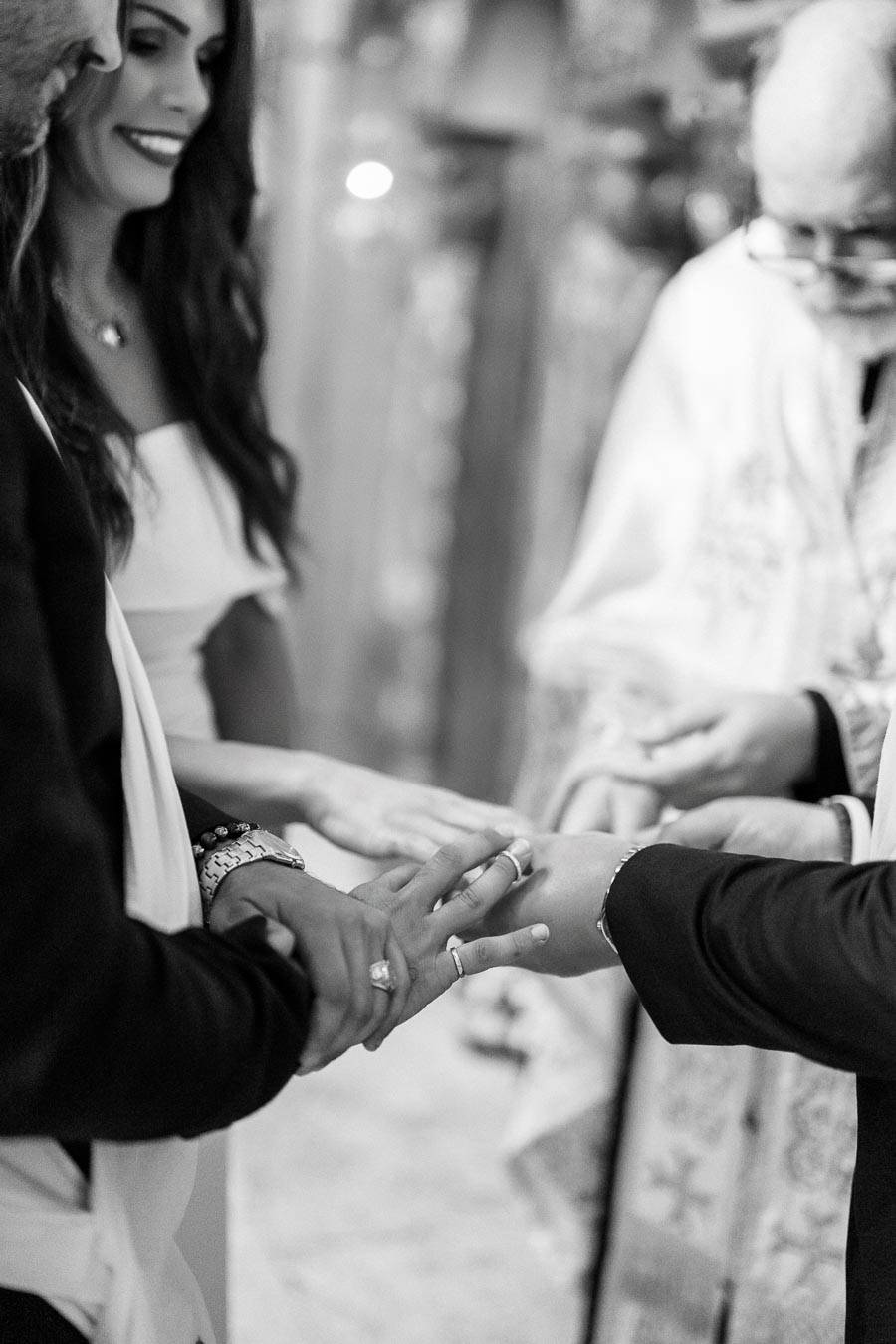 Black and white image of a wedding ceremony with a couple exchanging rings, guided by a priest.