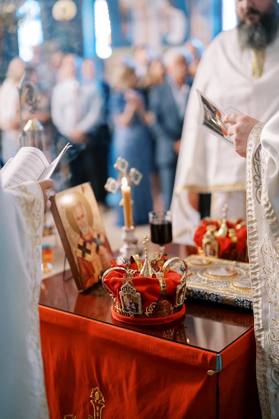 A traditional religious ceremony with ornate crowns and an icon on a table, surrounded by people wearing ceremonial garments inside a church.