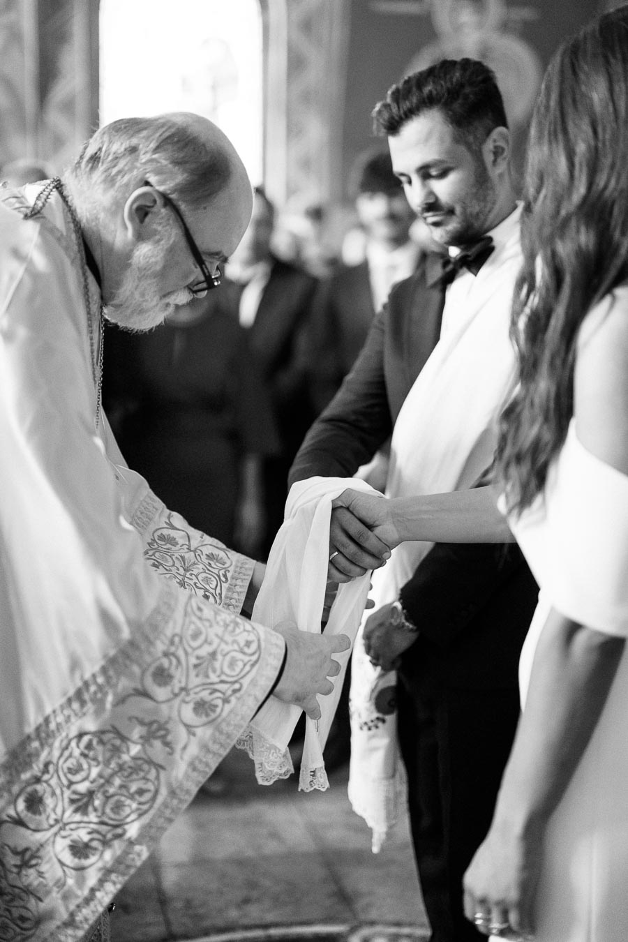 A priest wraps a cloth around the hands of a bride and groom during a traditional wedding ceremony in a church setting.