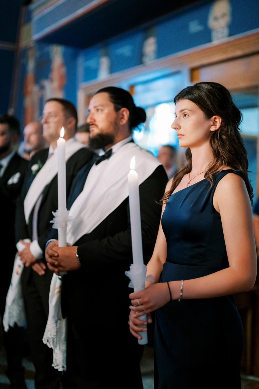 Formal ceremony with people holding tall white candles, wearing elegant attire.