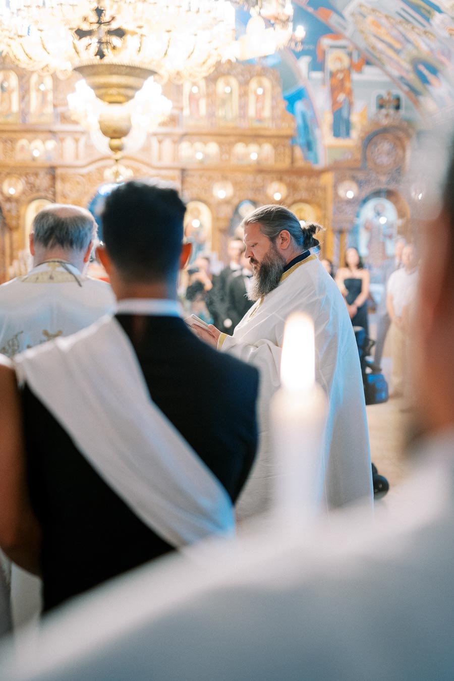 Priest conducting a ceremony inside an ornate church, with onlookers and intricate religious iconography in the background.