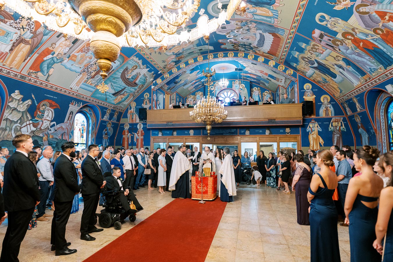 Orthodox wedding ceremony in a beautifully adorned church with vibrant murals, ornate chandeliers, and a gathered congregation.