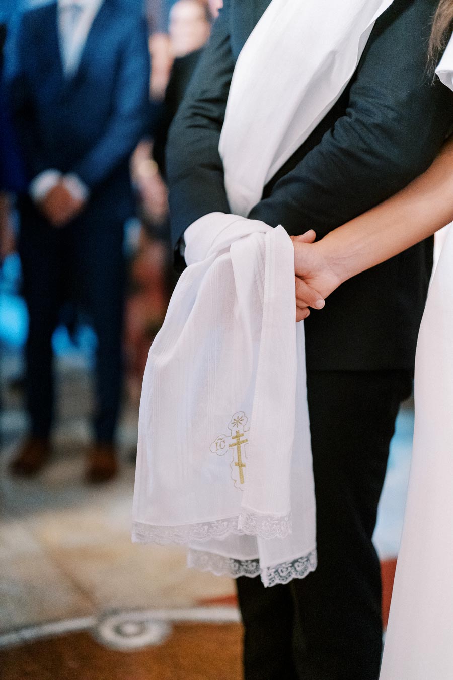 Close-up of a couple's hands tied with a white cloth during a wedding ceremony, symbolizing unity and commitment, with blurred guests in the background.
