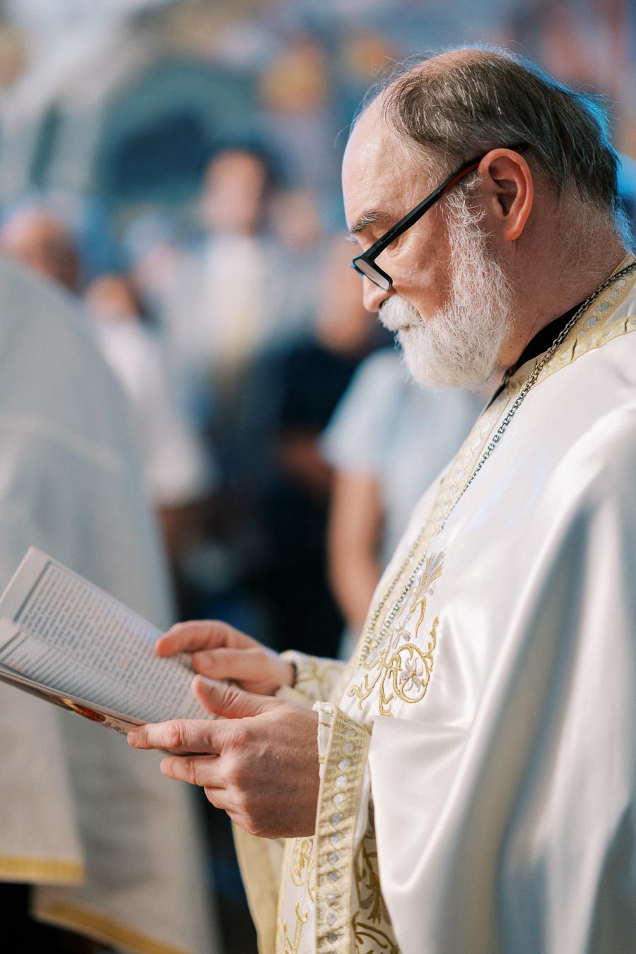 Elderly man in traditional religious robe reading a book during a church ceremony.
