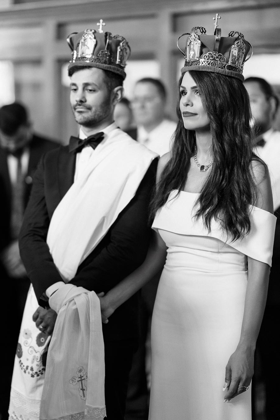 A couple in ceremonial attire wearing ornate crowns during a traditional wedding ceremony.
