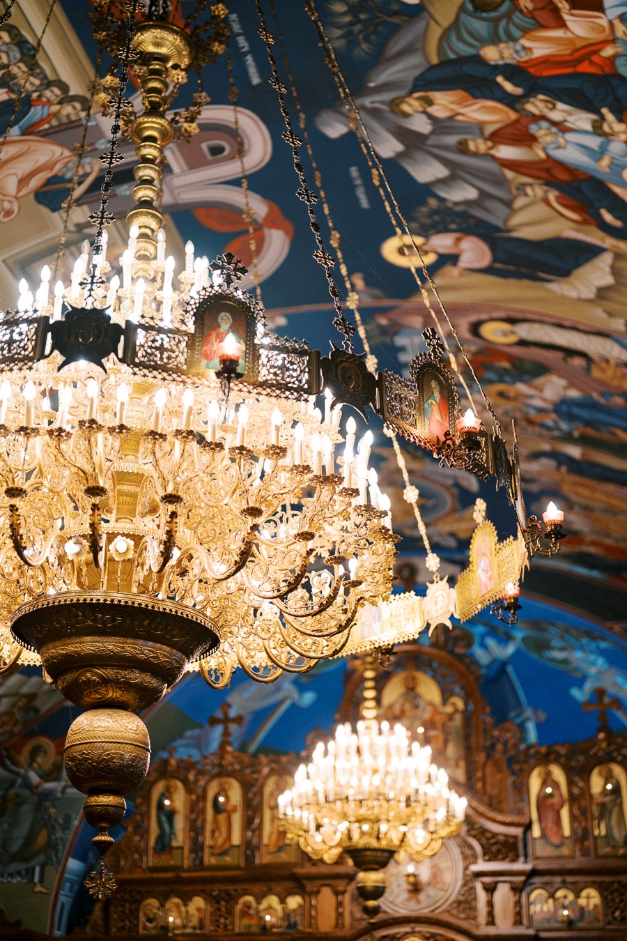 Ornate golden chandelier with candles hanging from a decorated ceiling with religious murals in a church interior.