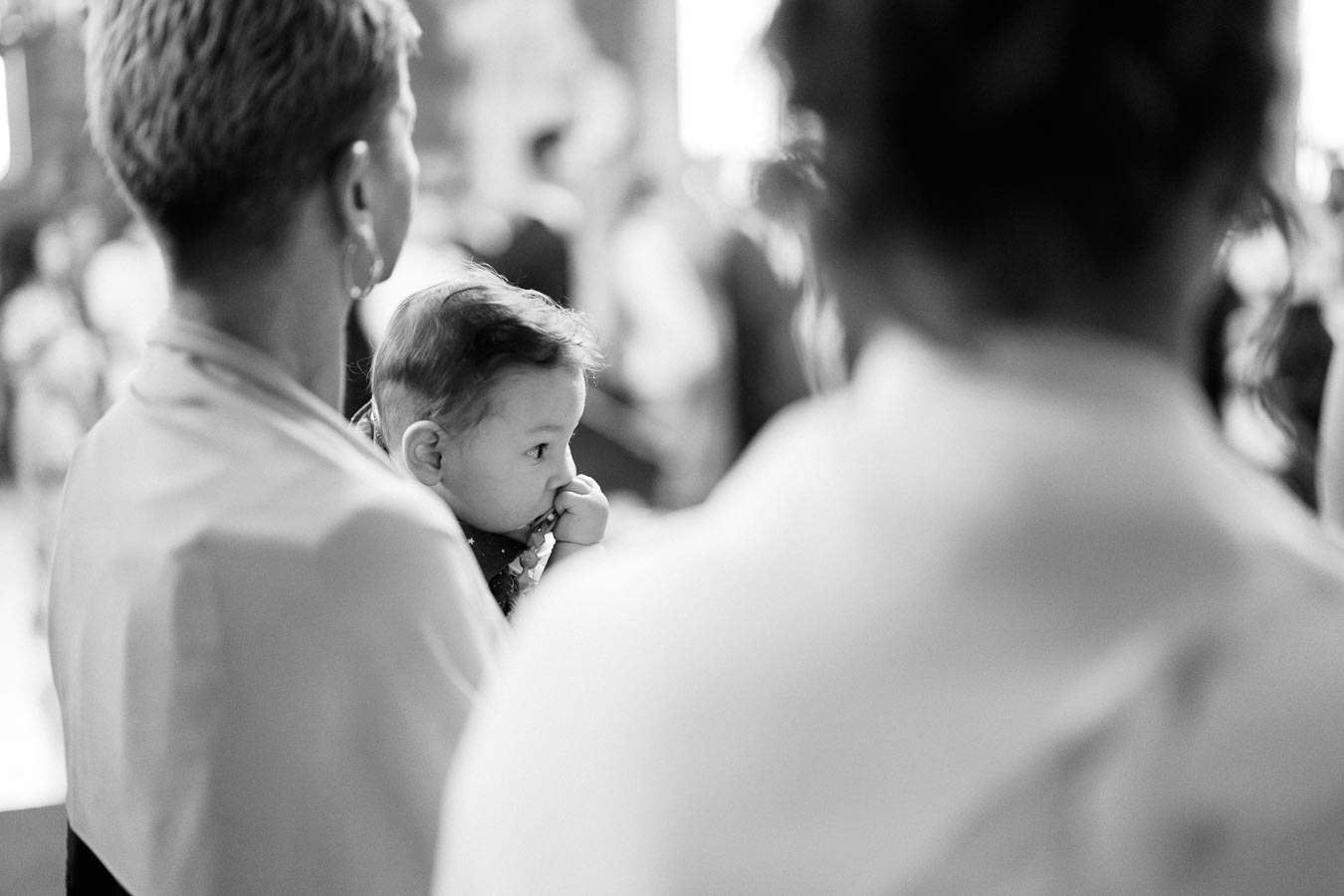 Black and white image of a thoughtful baby being held by an adult in a crowded event setting.
