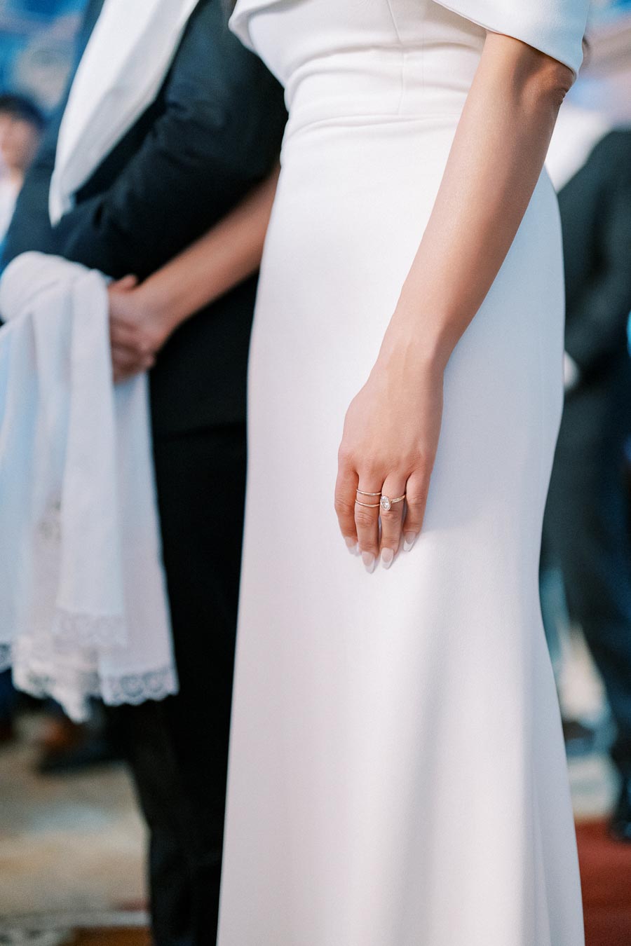 Close-up of a bride in an elegant white gown showcasing a diamond engagement ring during a wedding ceremony.