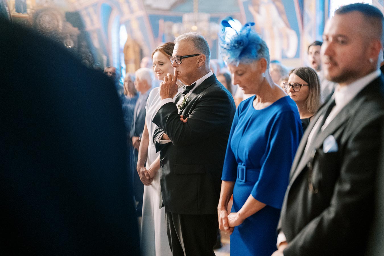 Guests attending a formal event, dressed elegantly, with women in dresses and men in suits, standing in a beautifully decorated indoor setting.