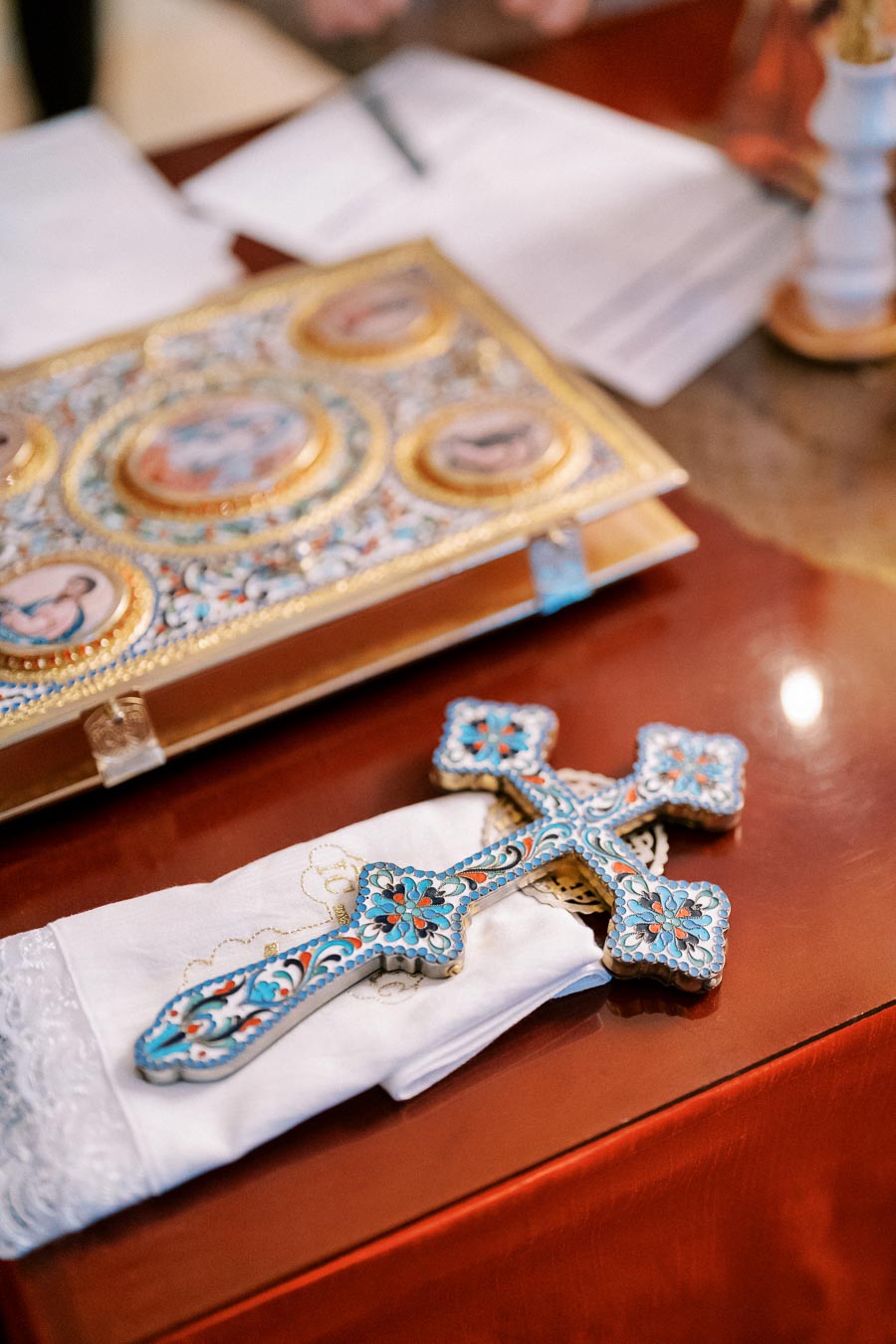 Decorative religious cross resting on a white cloth beside an ornate book with gold and colorful detailing, on a wooden surface.