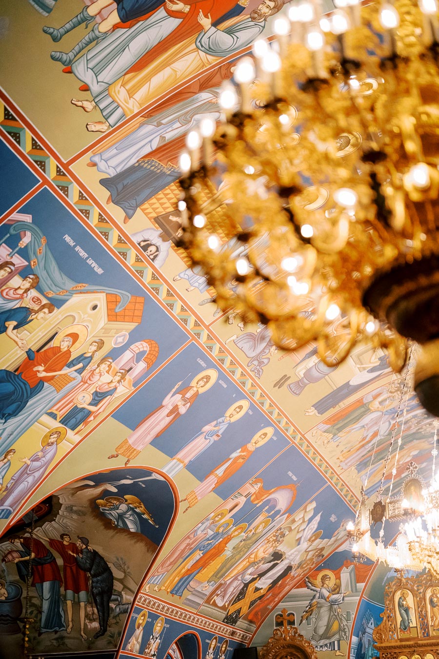 Ornate interior of a church featuring vibrant religious frescoes and a golden chandelier, showcasing traditional iconography and intricate artwork.