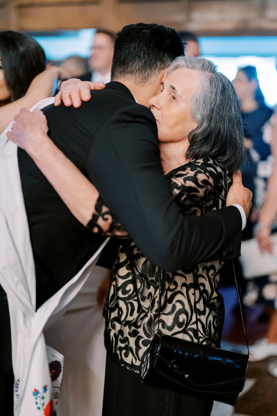 Elderly woman hugging a man in a suit at a formal event, conveying warmth and affection.