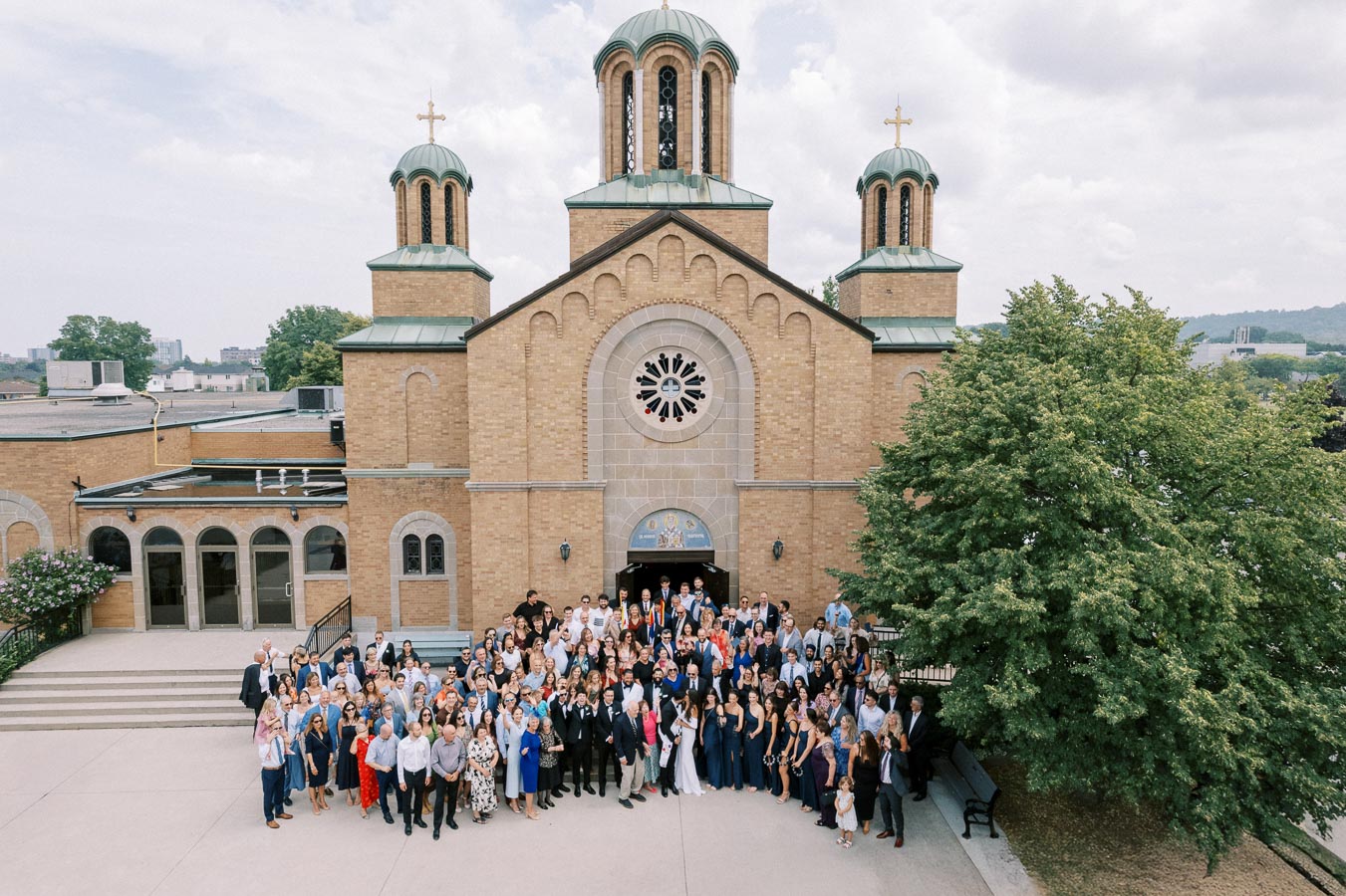 Large group of people gathered outside a historic church with domed towers, engaging in a community event on a sunny day.