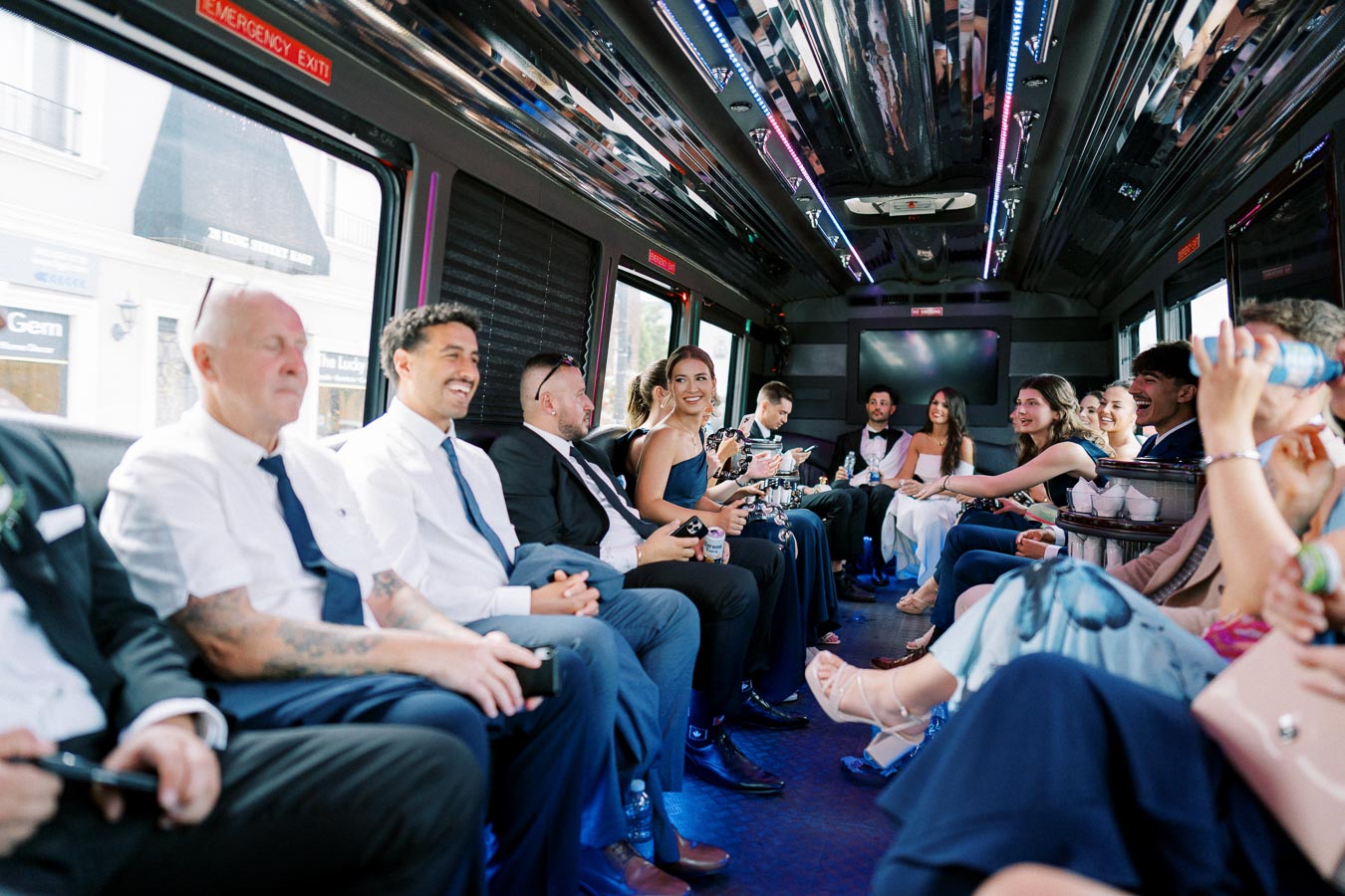 A group of well-dressed people smiling and socializing inside a party bus with colorful lighting, suggesting a celebratory or event setting.
